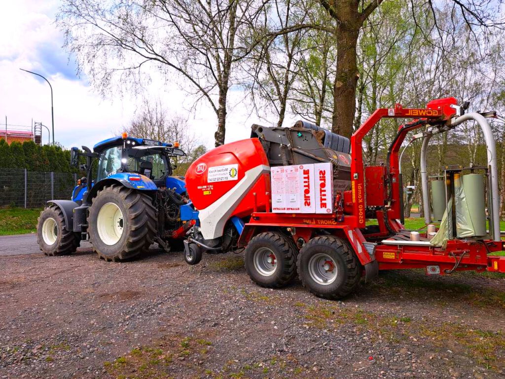 New Holland Traktor fährt vom Hof mit eine Rundballenpresse