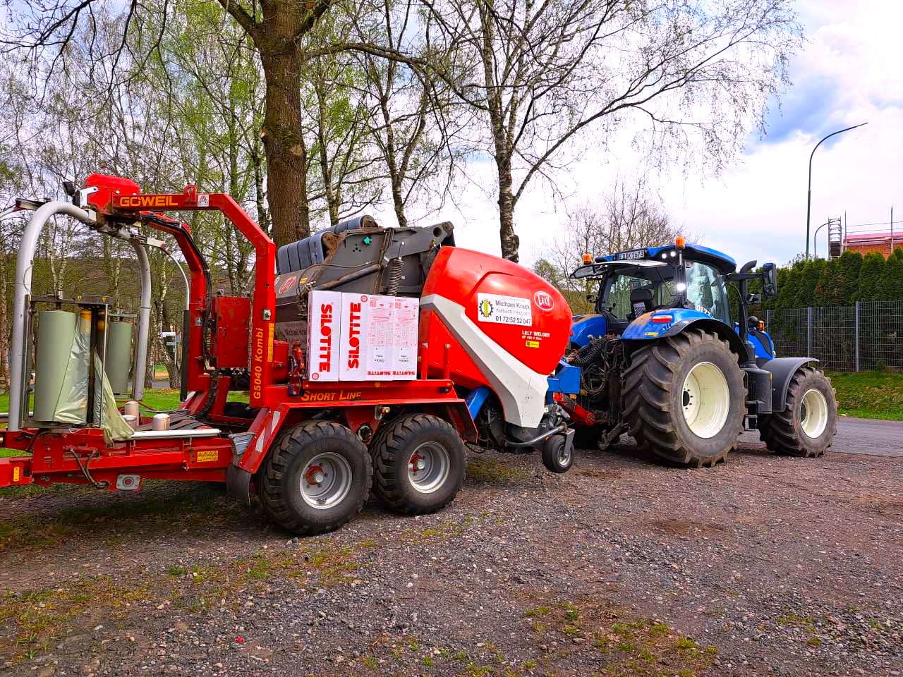 New Holland Traktor fährt vom Hof mit eine Rundballenpresse
