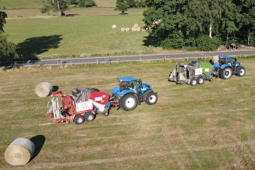 2 New Holland Traktoren sind auf der Heuwiesemit einer roten und einer grünen Rundballenpresse